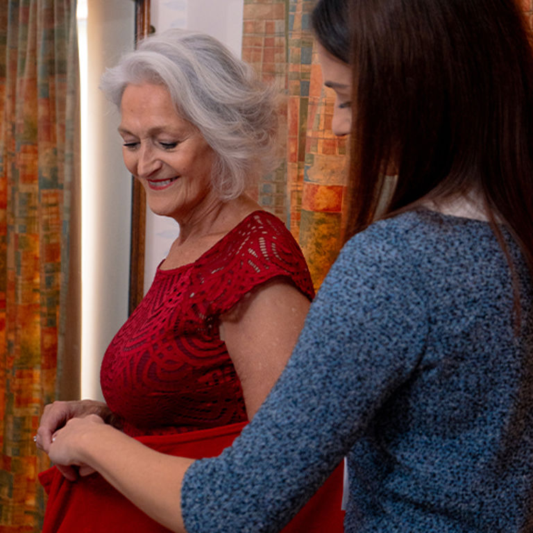 Caregiver assisting older woman with dressing at home as part of personal care support