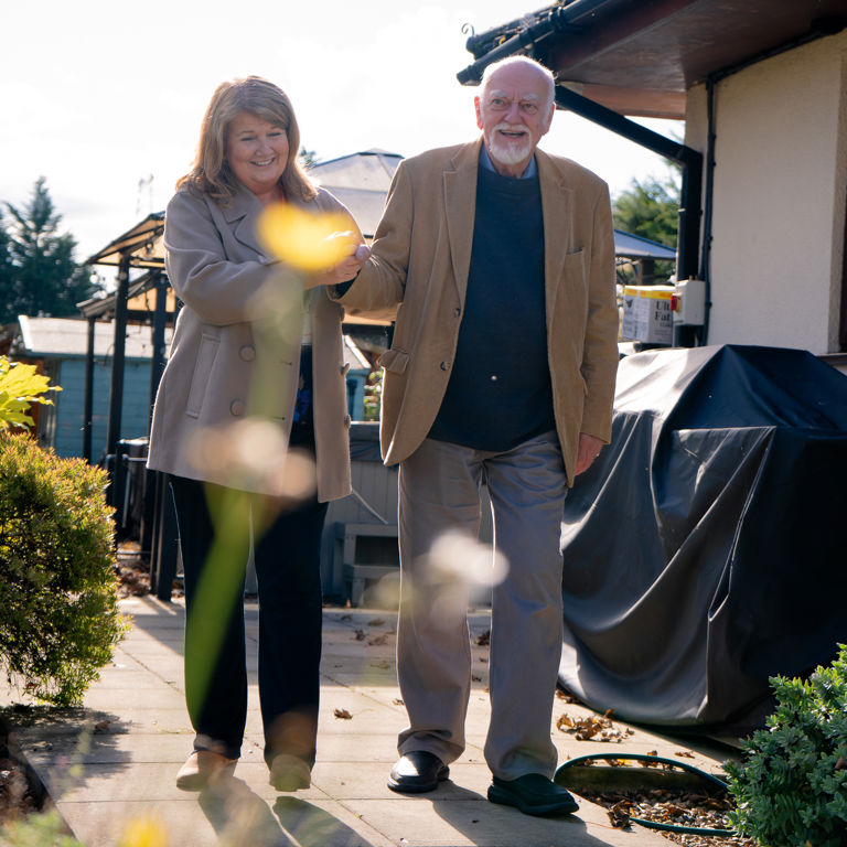 Client and Carer walking through garden and smiling