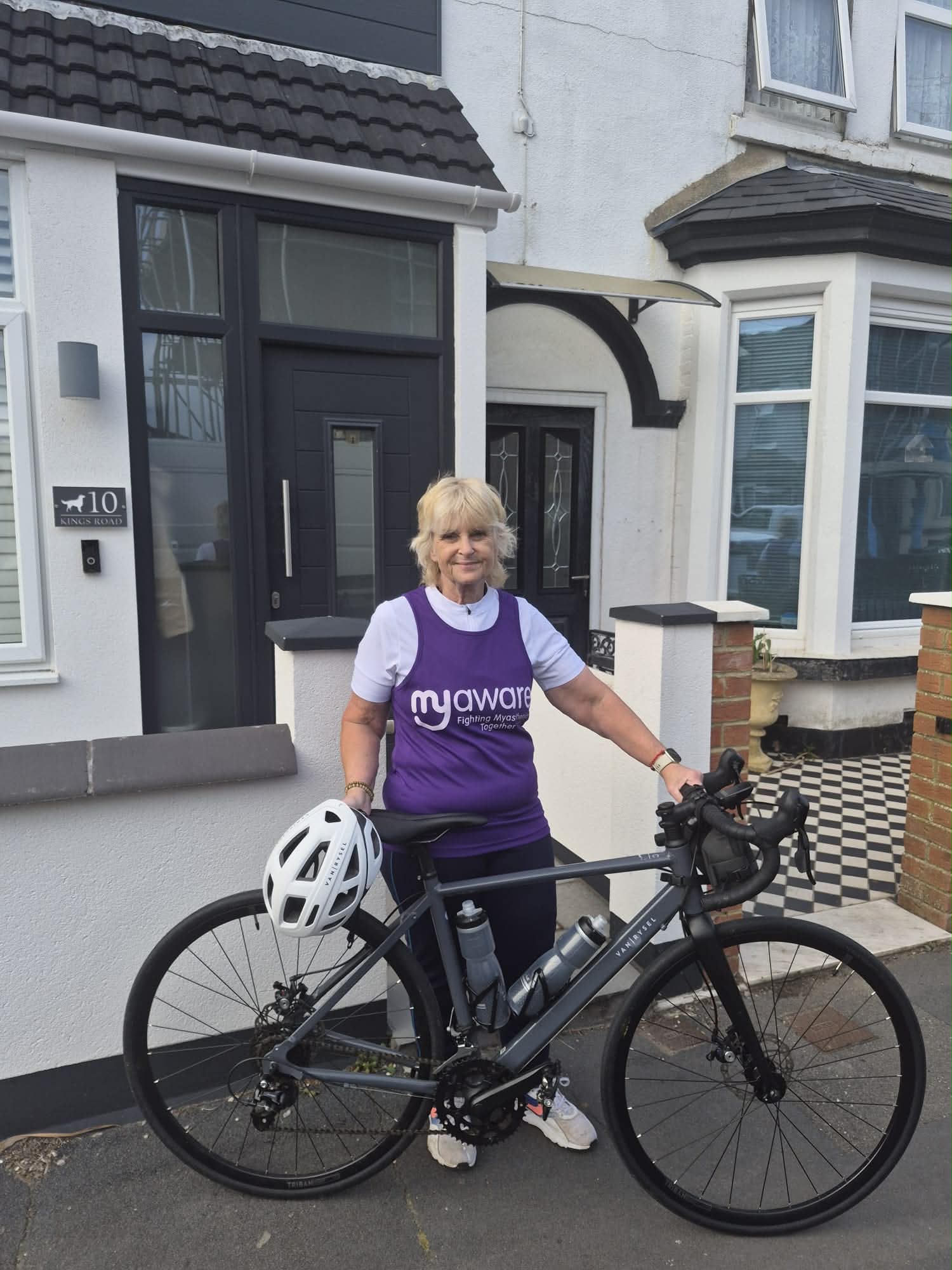 Julie standing beside her bicycle, smiling and holding the handlebars during her charity ride preparation for Myasthenia Gravis awareness.