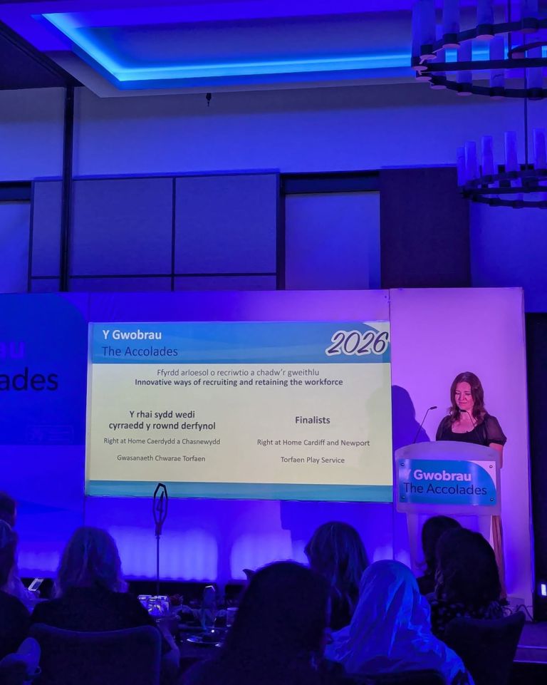 The stage at Social Care Wales accolades with a screen showing that Right at Home Cardiff and Newport and Torfaen Play Service were nominated in the category Innovative ways of recruiting and retaining the workforce