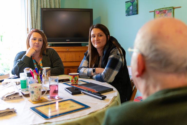 Caregiver and Daughter sitting with older man at home discussing care and support around dining table