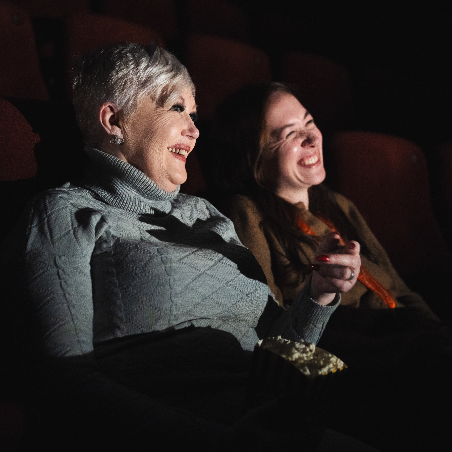 A carer and client laughing at a scene from a film at the cinema