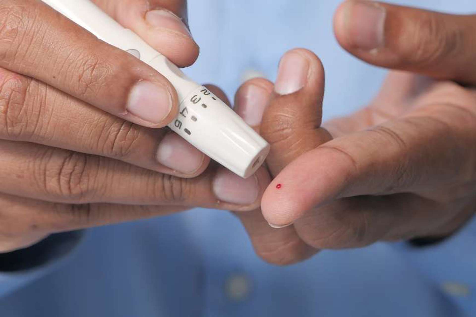 close-up-of-a-gentleman-using-a-finger-prick-testing-device-helped-by-a-home-caregiver-from-right-at-home-cheshire-east-stockport