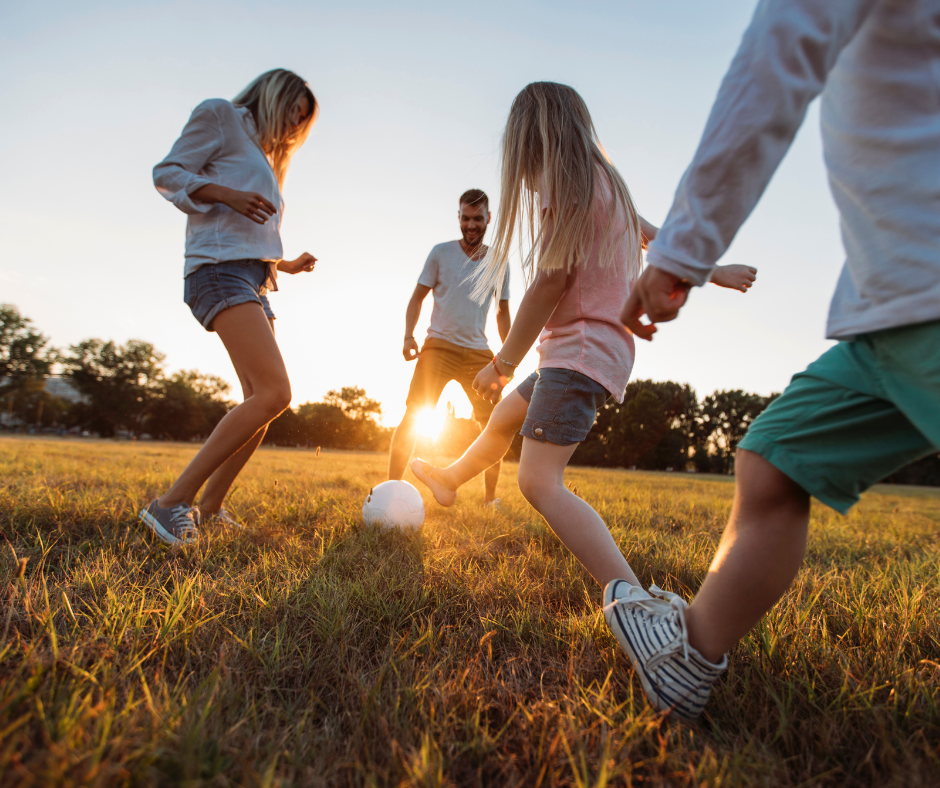 Family playing football in a field with sunset