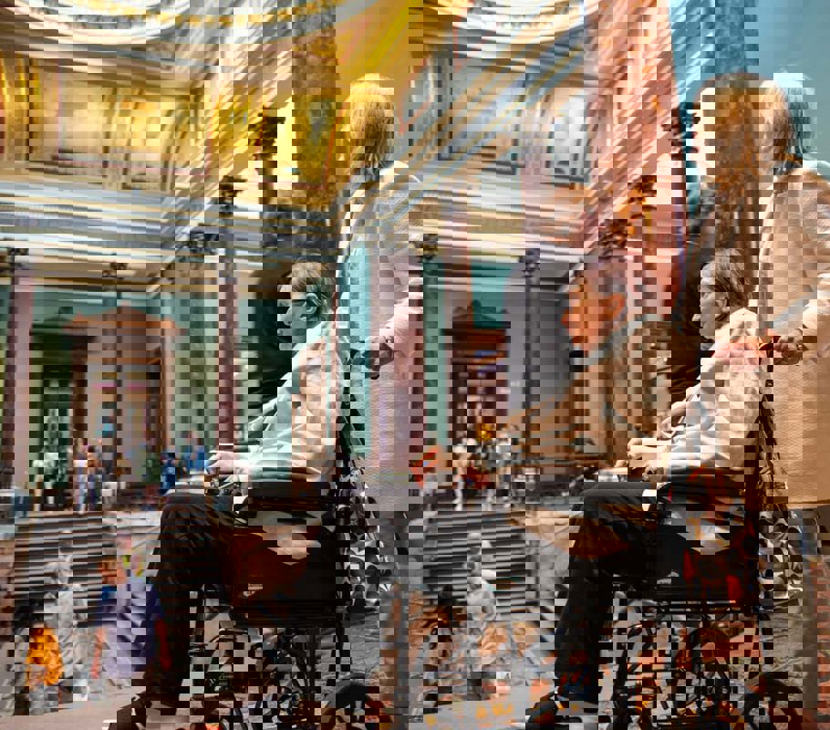 Client in wheelchair being pushed by CareGiver through a museum