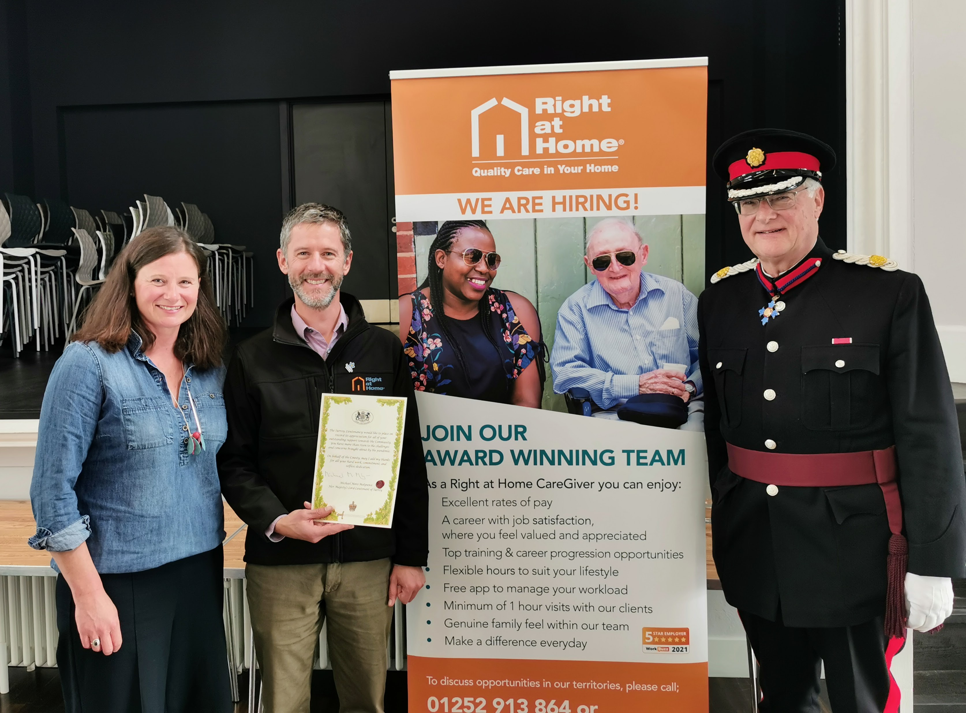 Smiling man and woman with a certificate. Man in military uniform on right of image.