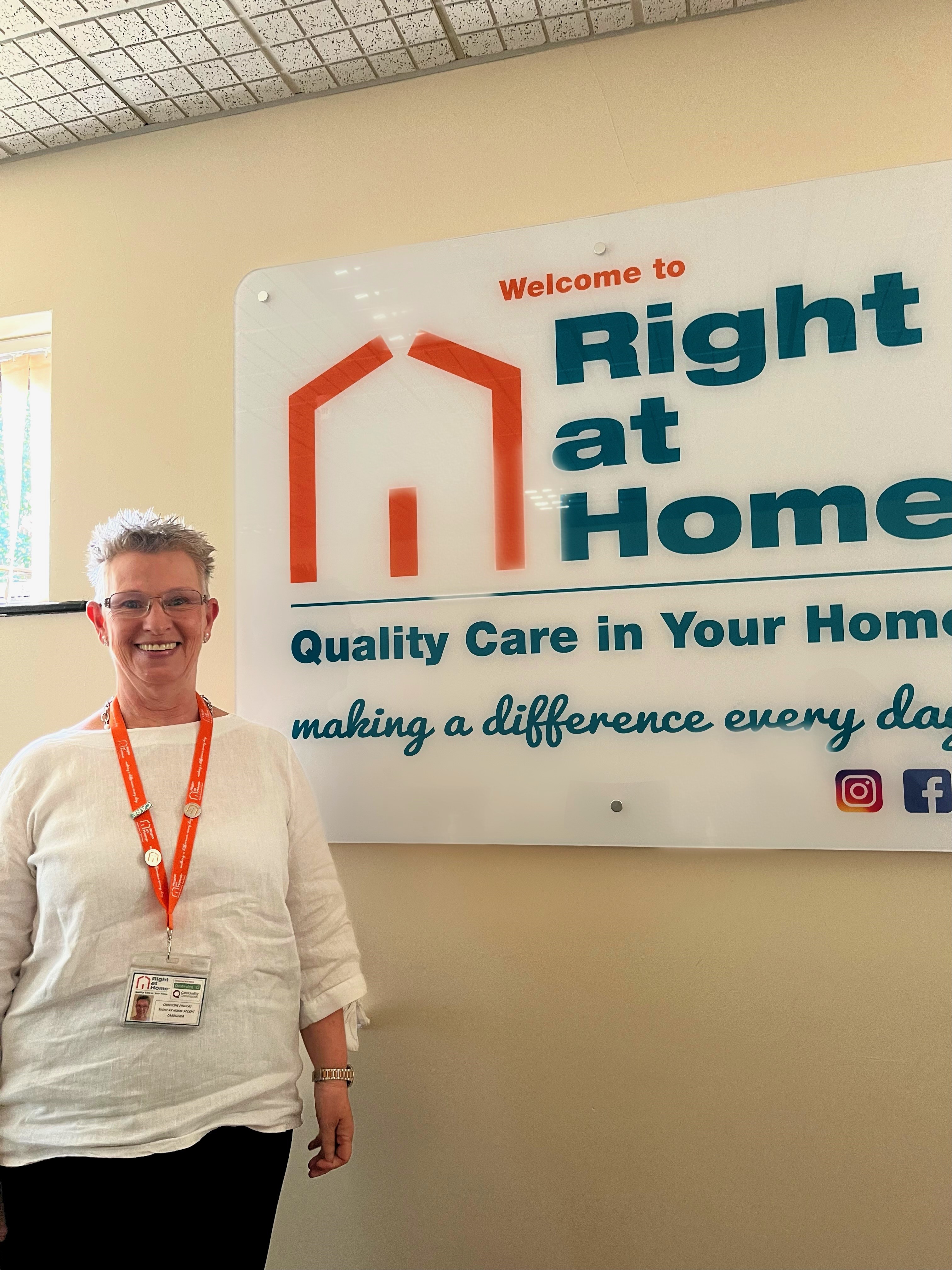 Smiling lady infront of white wall and sign, with her work lanyard on