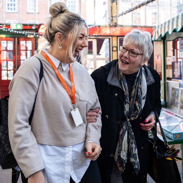 Client and Carer linking arms and laughing in market