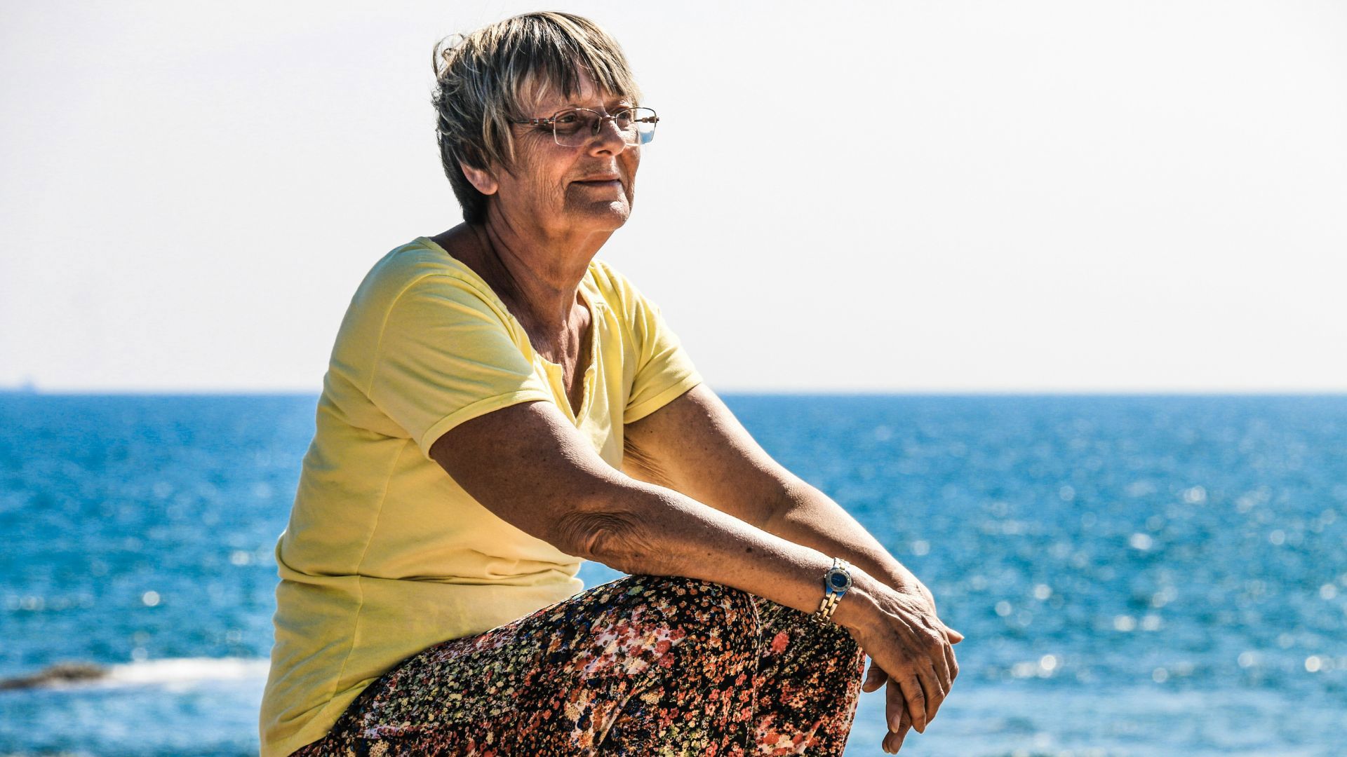 older woman sitting by the water in the sun