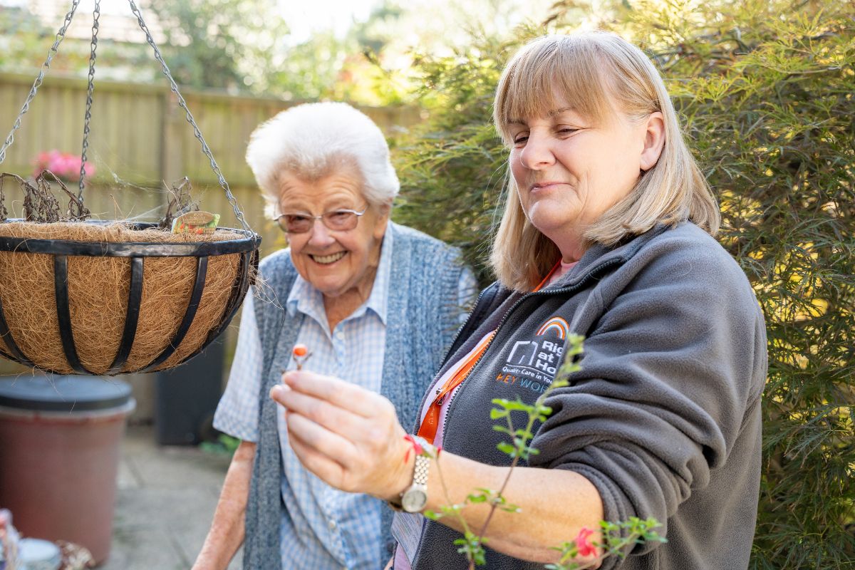 Carer showing the client a small flower outside the house,