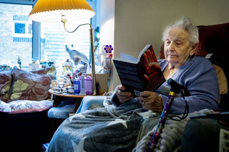 elderly-lady-sat-at-home-enjoying-reading-a-book-in-her-own-armchair-in-stockport